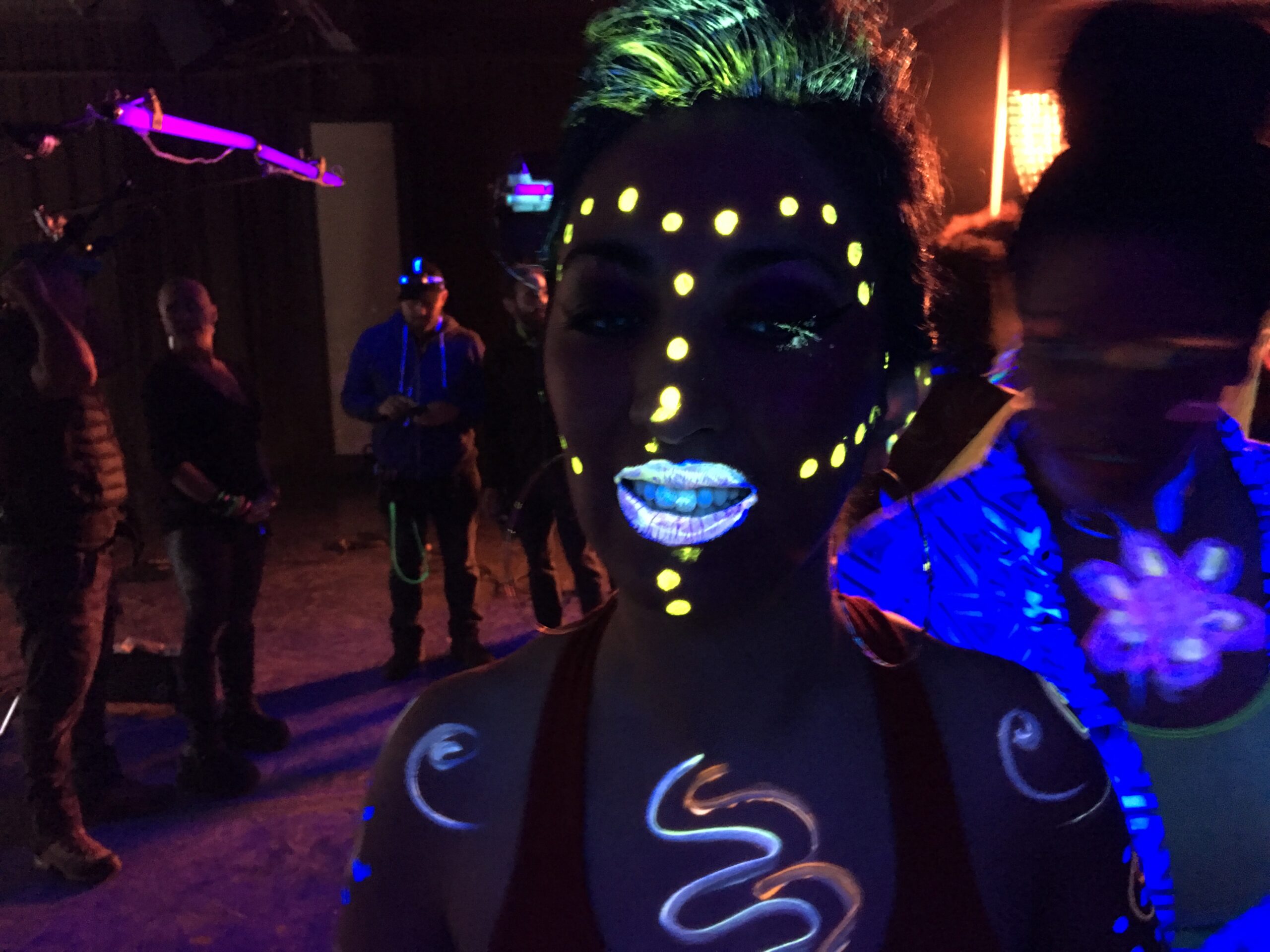 Music Video Scene featuring a dancer with glowing bodypaint seen in neon light. In the background you can see the film crew and neon light tubes.