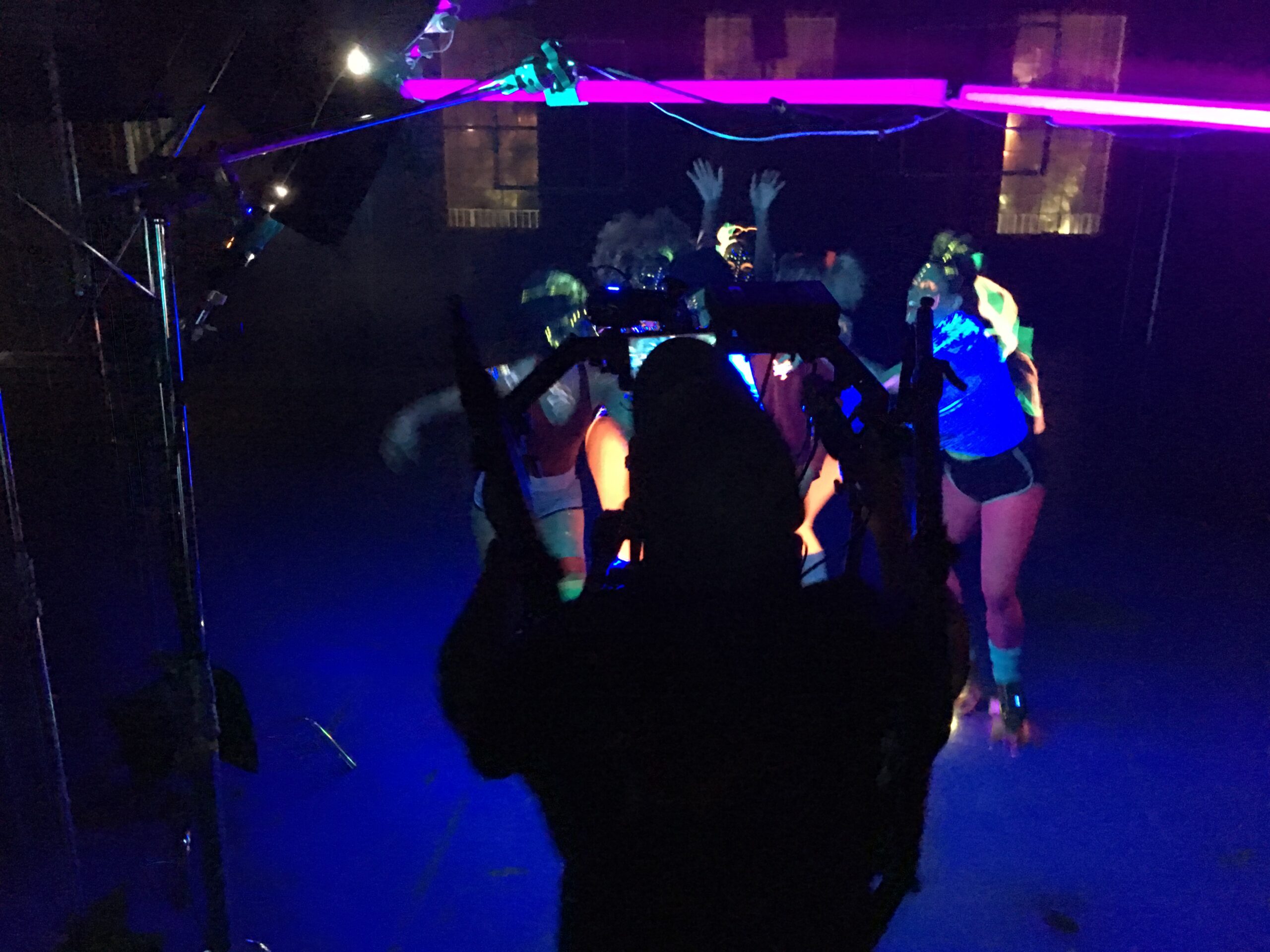 Music Video filming of a group of dancers using neon lights. Viewed from behind the cameraman showing some neon tube lights.